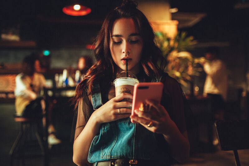 Woman at a cafe drinking coffee holding a smartphone.jpg