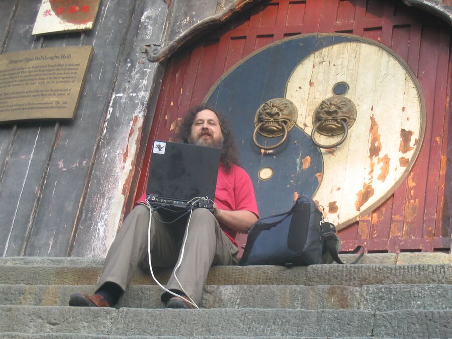 Richard Stallman working on his laptop outside something.jpg